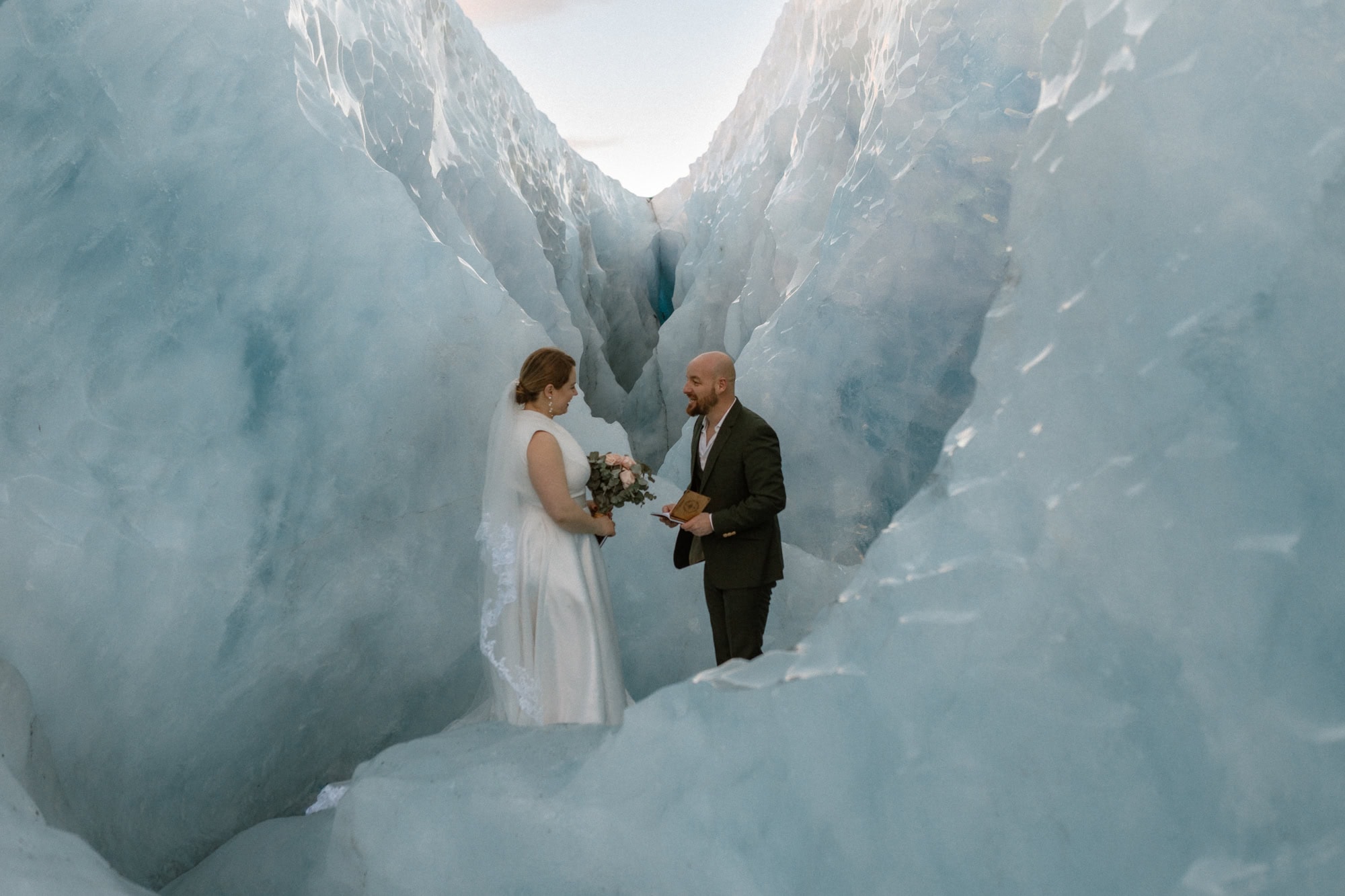 Elope in a stunning Iceland glacier crevasse with a couple exchanging vows during a unique adventure. Perfect for adventurous couples seeking a memorable wedding experience.
