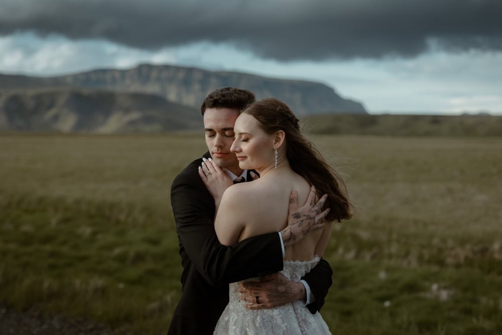 Intimate Iceland elopement with a couple embracing outdoors against scenic mountains and cloudy sky.